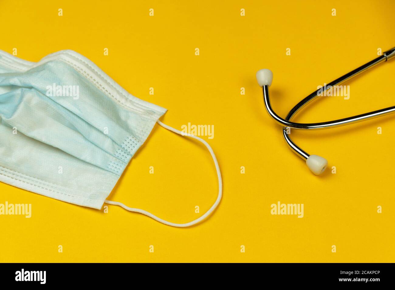 stethoscope with blue surgical mask for corona virus protection on yellow paper health care background Stock Photo