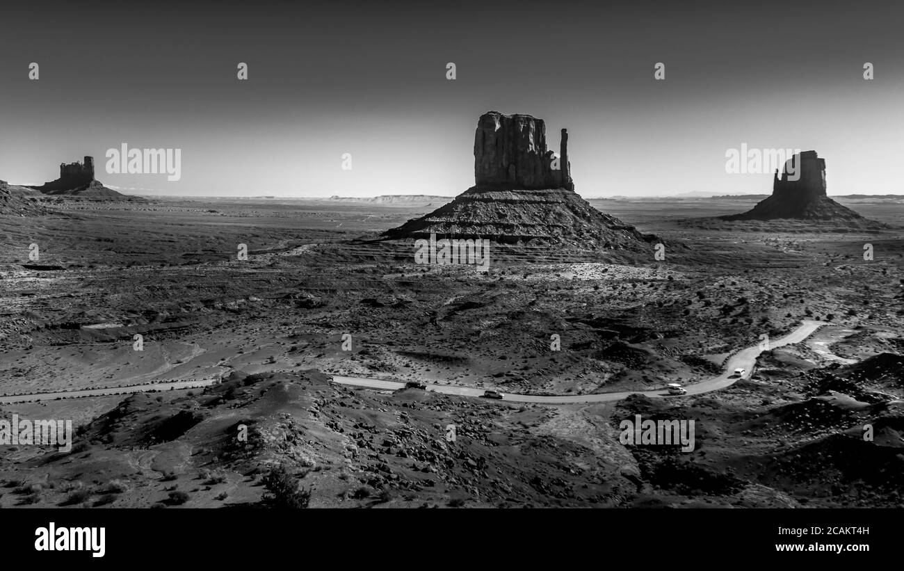 Black and White Photo showing the gravel road winding around East and West Mitten Buttes in the desert landscape in Monument Valley, Utah, USA Stock Photo