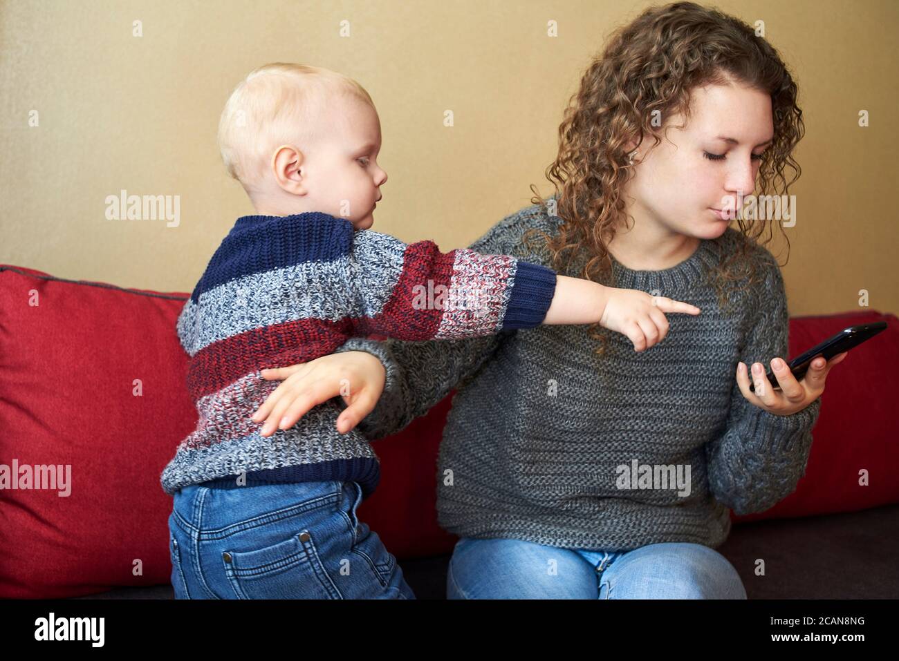 Mother is indifferent to her little son, mom looks at the smartphone, the child needs attention. The theme of parent-child relationships. Stock Photo