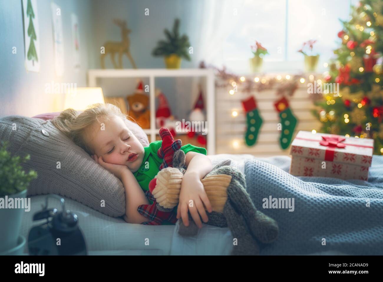 Merry Christmas and Happy Holiday! Cute little child girl sleeping in the bed near tree at home. Stock Photo