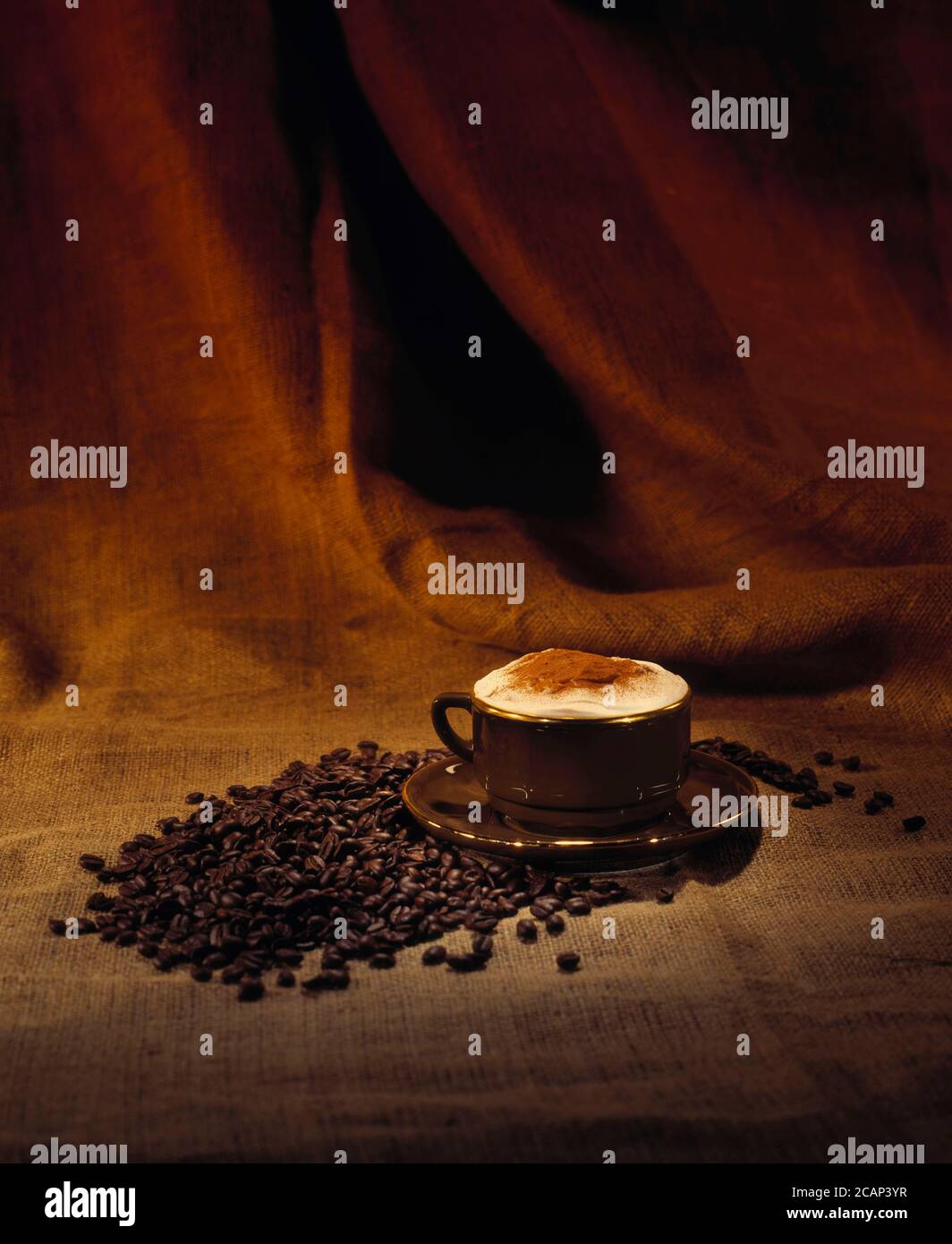 Cappuccino coffee in a brown cup with gold rim on a brown hessian background with whole coffee beans space for caption portrait format Stock Photo