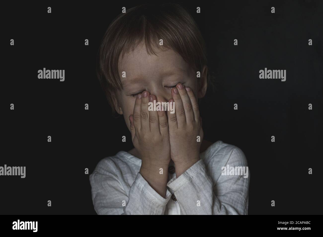 Portrait of a scared little boy child. The kid covered his mouth with his hands, closed his eyes. The concept of stuttering, silence due to stress and Stock Photo