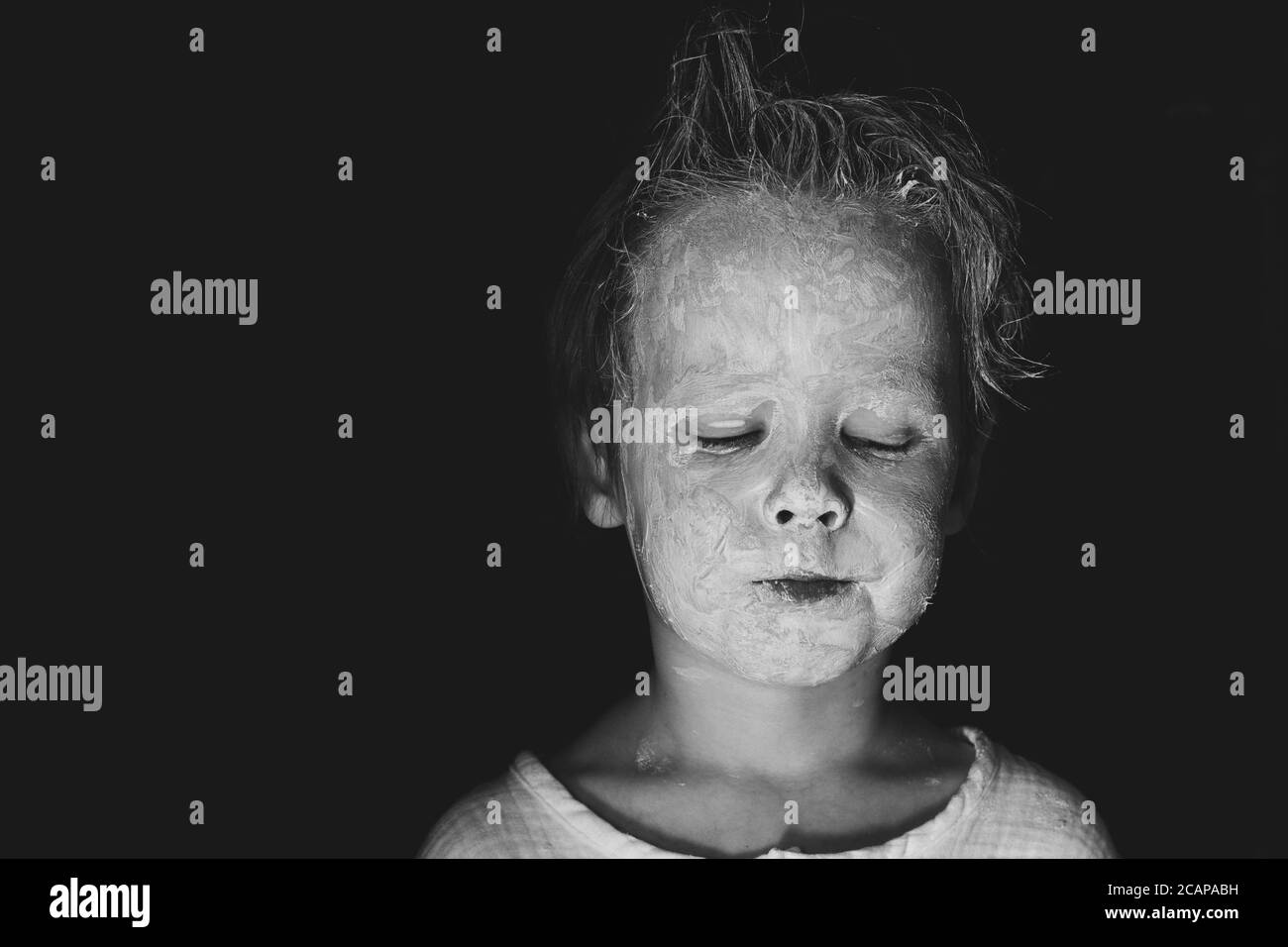 scary little child with a smeared white clay or make-up face monochrome black and white. Stock Photo