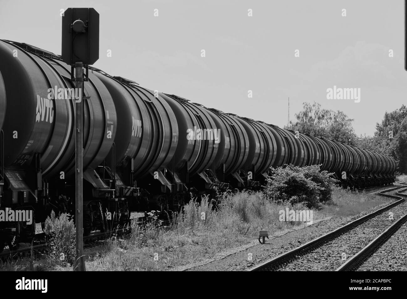 Magdeburg, Germany, June 27., 2020: Long train with tank wagons behind each other in a row on a track next to empty rails, black and white Stock Photo