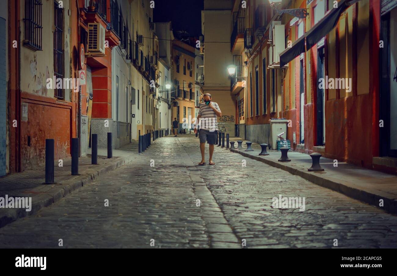 Unrecognizable man wearing mask and walking in a street at night (Calle Pacheco y Nuñez del Prado) in Seville, Spain Stock Photo