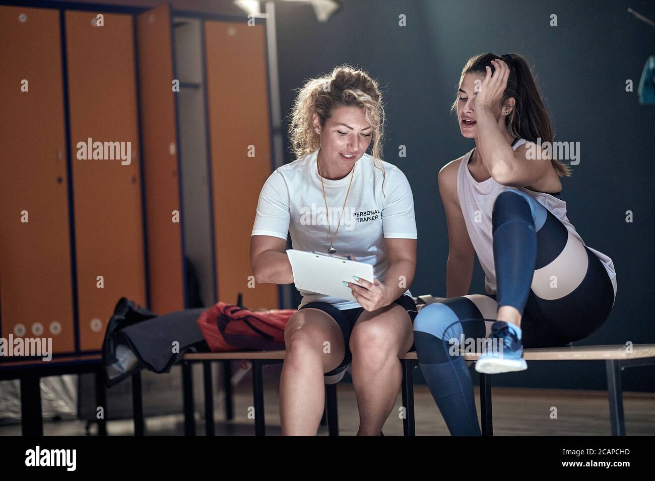 Female personal trainer and young fitness girl in a talk in a locker room Stock Photo