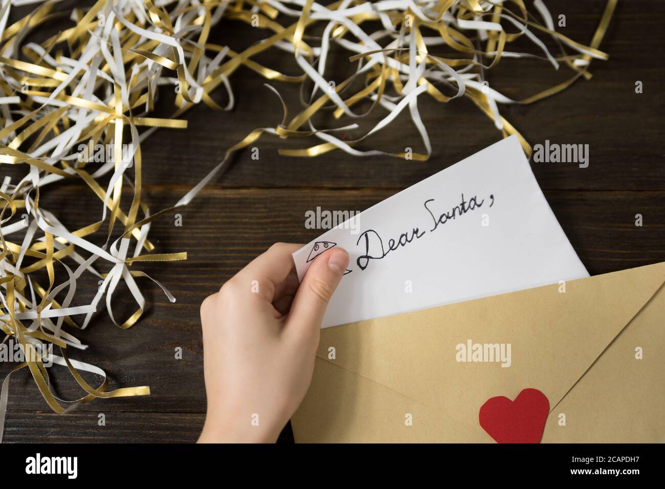 Children's hands put a letter for Santa in an envelope. Wooden background. Close-up Stock Photo