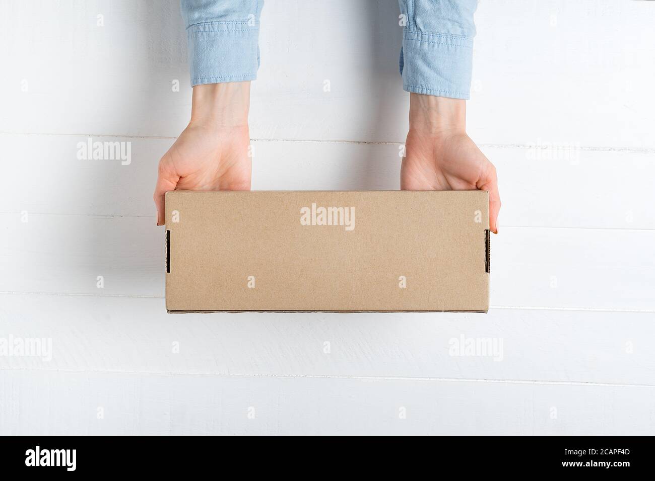 Rectangular cardboard box in female hands. Top view, white background Stock Photo
