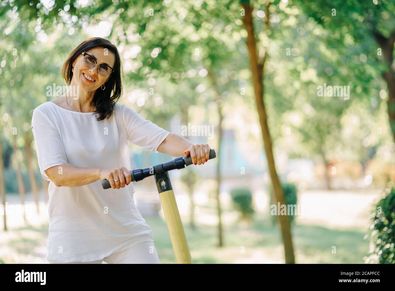 Close up Joyful adorable senior woman using a scooter while riding in the park. Modern woman, a new generation. Healthy cheerful senior retired lady Stock Photo