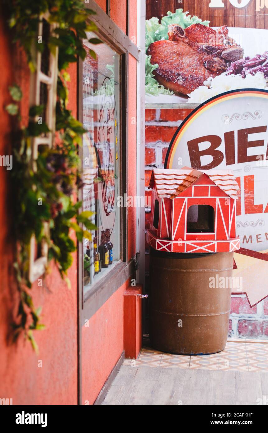 Side view of a shop display with red walls and a trash bin shaped as a lovely red colonial house in Vila Germânica, Blumenau - Brazil during the after Stock Photo