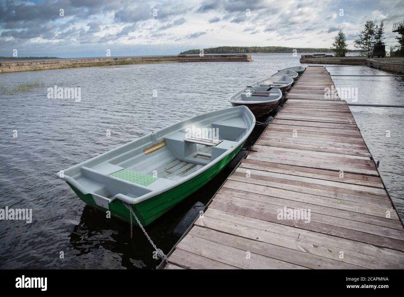 Green empty boats on the lake along the wooden pier, cloudy autumn sky against the background. Stock Photo