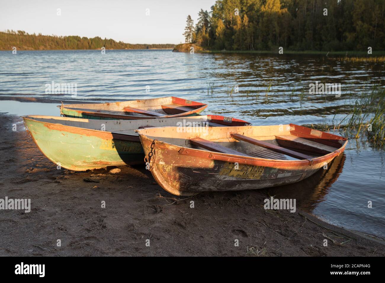 Old shabby wooden fishing colorful boats on the lake shore during sunset, autumn forest on background. Calm sunset on the nature Stock Photo