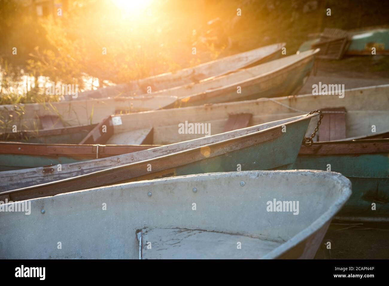 Closeup of old shabby wooden fishing colorful boats and boat bow during a sunset with sun rays, selective soft focus. Calm sunset on the nature Stock Photo