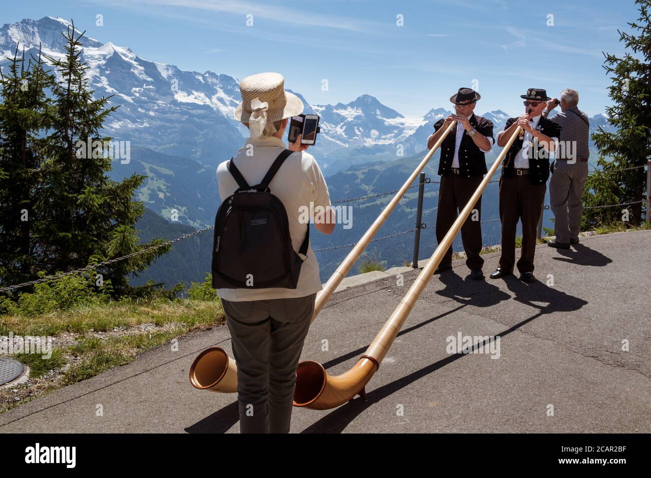Schynige Platte, Bernese Oberland, Switzerland - August 1 2019 : 2 Alpenhorn players in traditional swiss outfit filmed by female tourist on mobile ph Stock Photo
