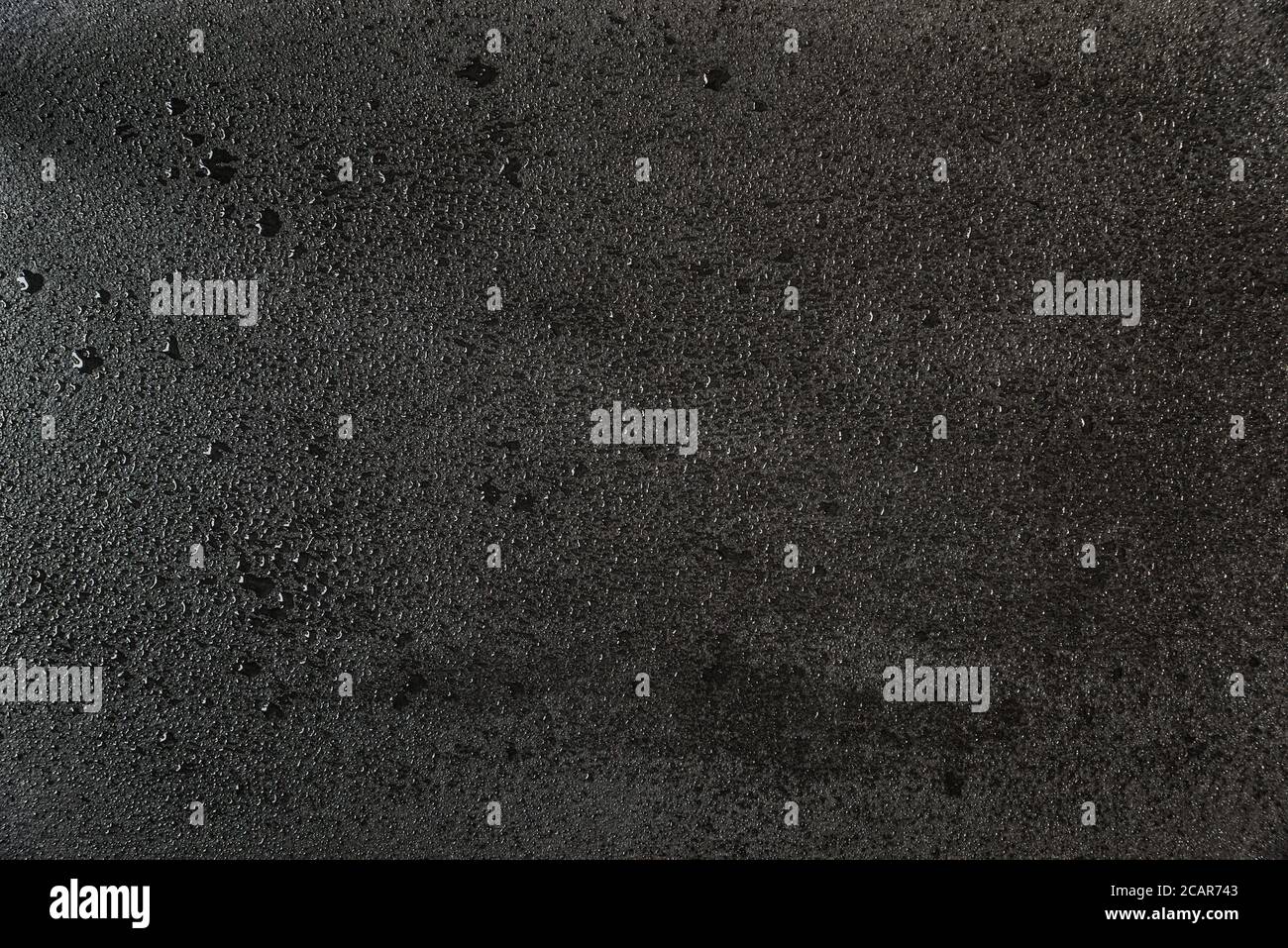 The rough surface of black slate stone, covered with small drops of water. Abstract background Stock Photo