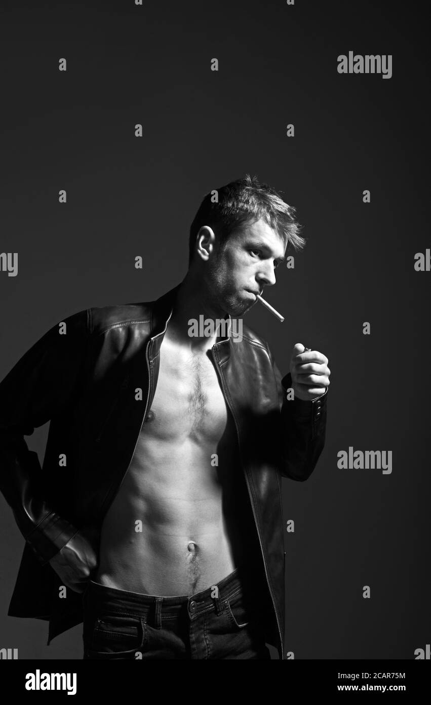 Portrait of a rebel type guy in classic leather jacket with cigarette in mouth against dark