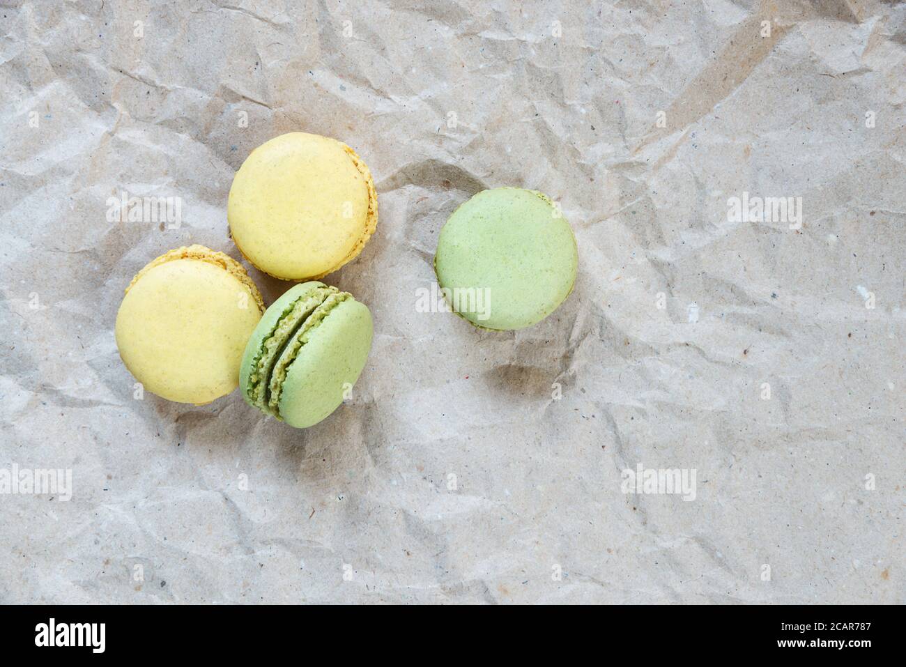 Green and yellow almond cookies (macaroons) on the background of crumpled craft paper, top view Stock Photo