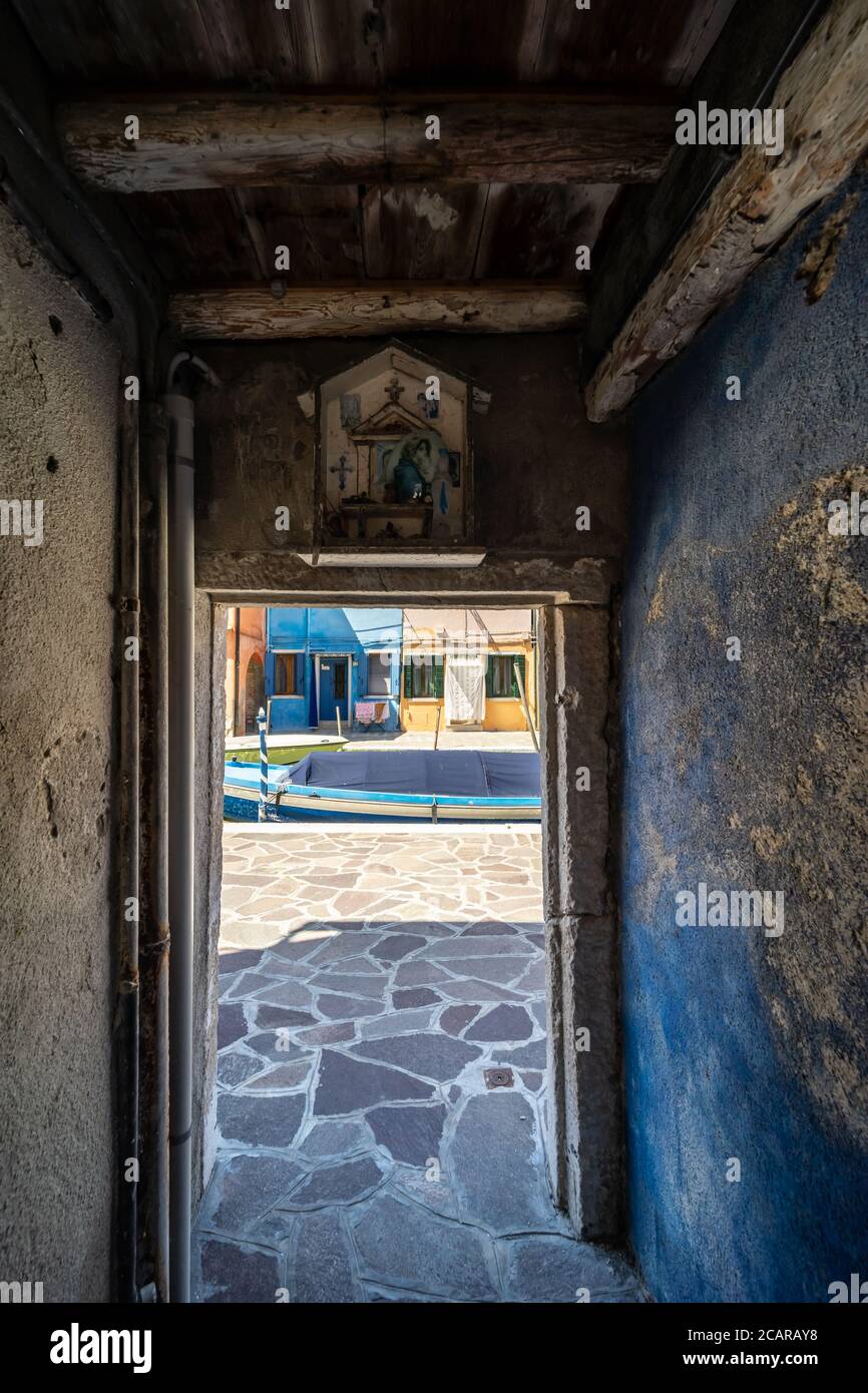 Burano island, Venetian Lagoon, Venice, Italy, a narrow passage between the typical coloured homes and a votive effigy in the town centre Stock Photo