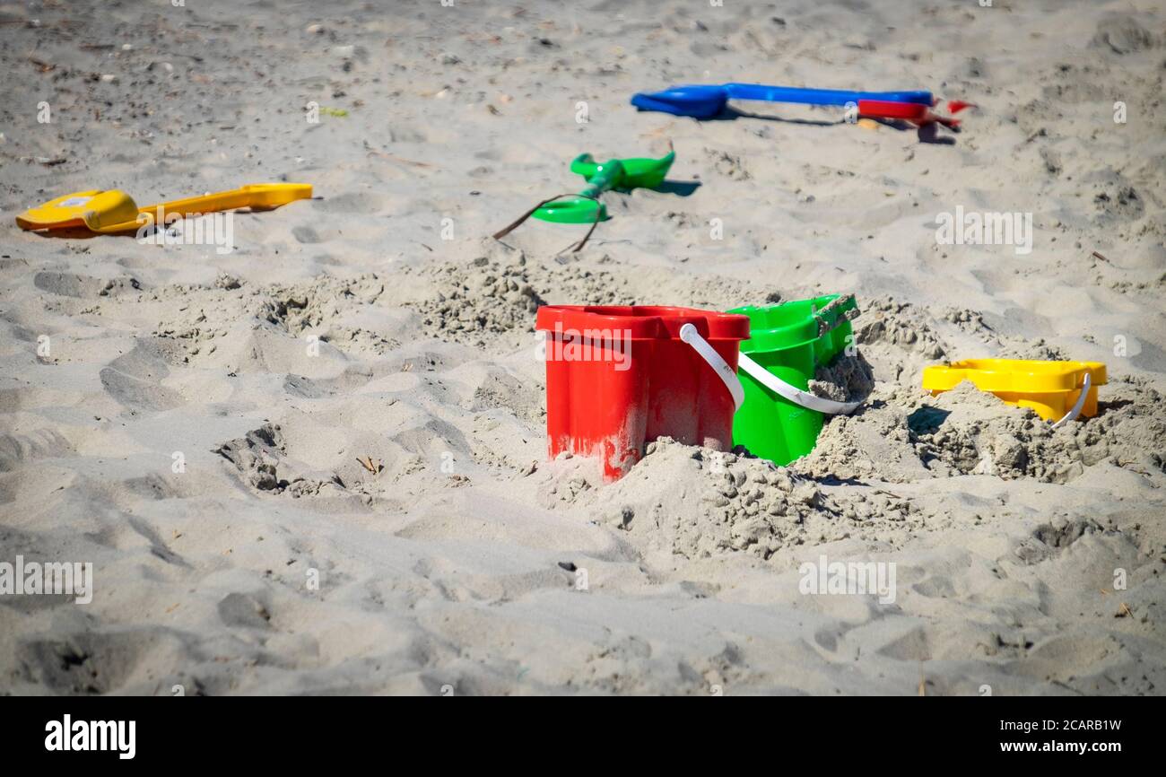 Colourful buckets and spades left laying on a sandy beach Stock Photo