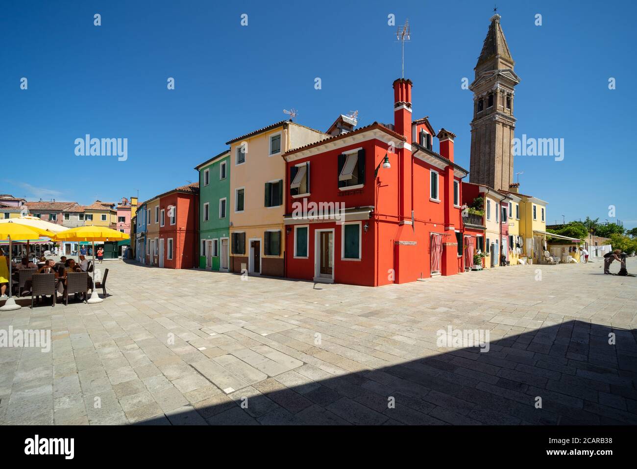 Burano island, Venetian Lagoon, Venice, Italy, central square with coloured homes, outdoor bars, and the leaning tower of the San Martino church Stock Photo