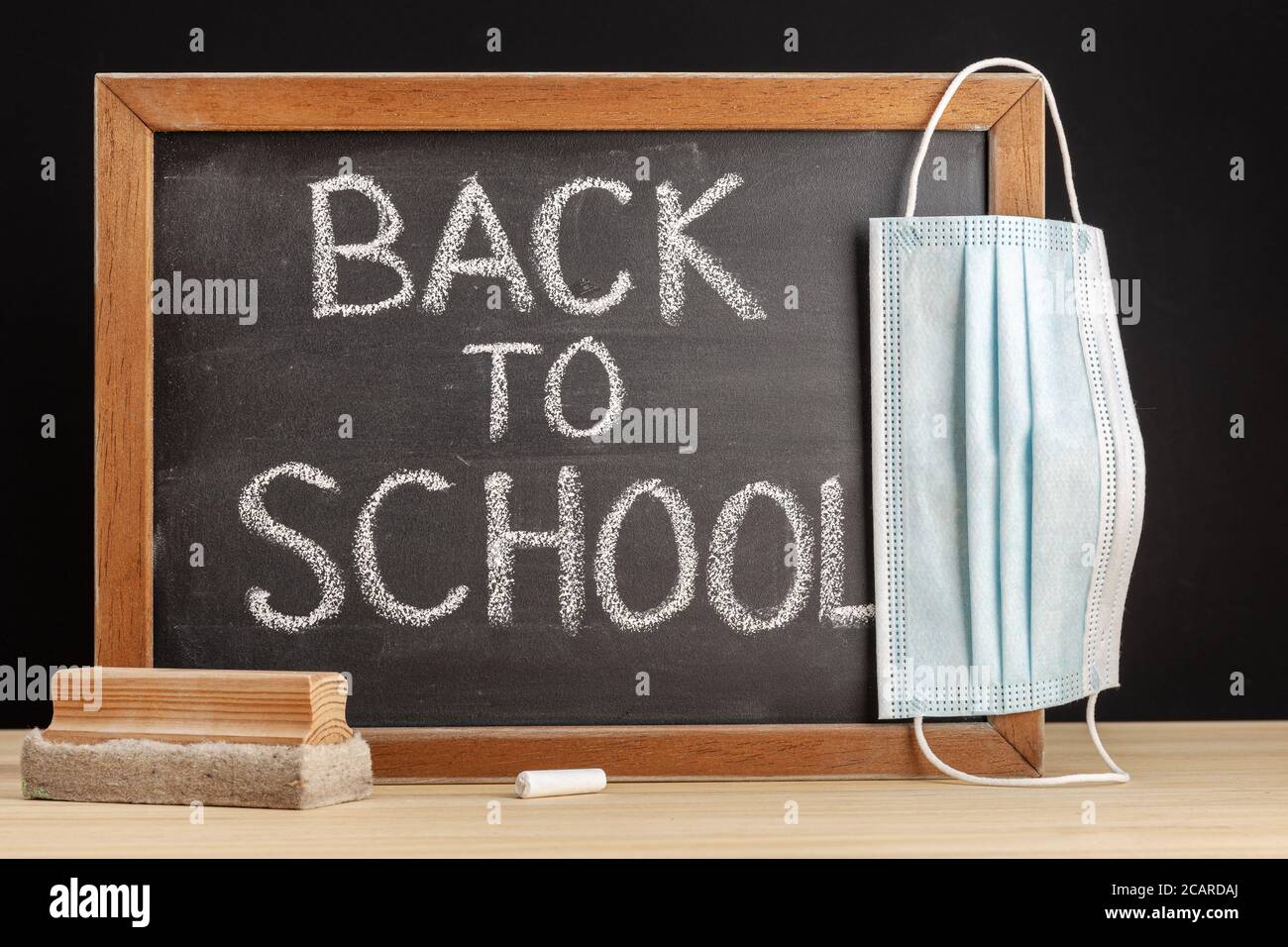 Return to school during covid-19 concept . Chalkboard with handwritten text and face mask hanging on table Stock Photo