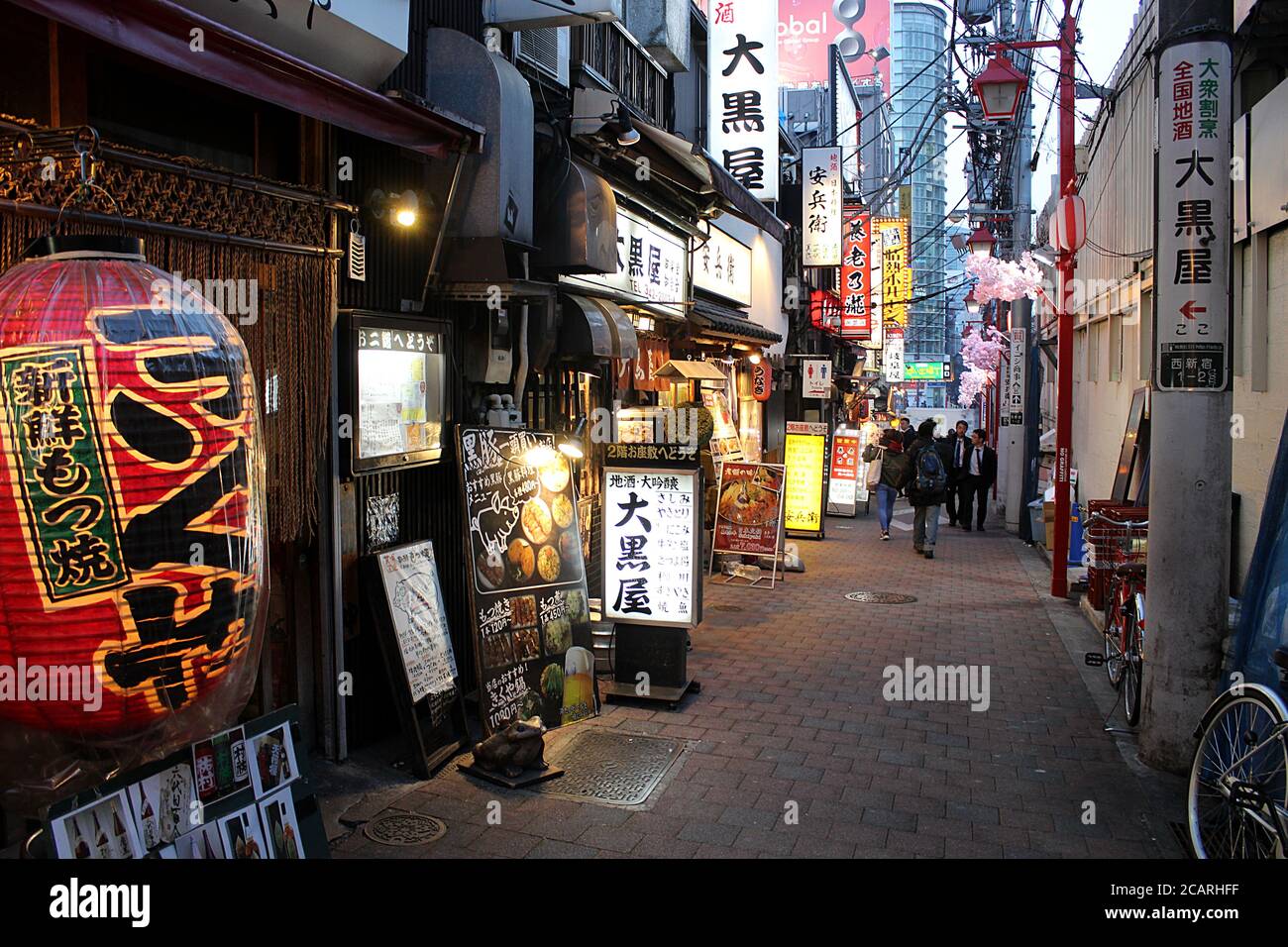 Tokyo, Japan - 13 March 2018: Illuminated alleyway with bars and izakayas (pub for after-work drinking) in the evening with few people walking by. Stock Photo