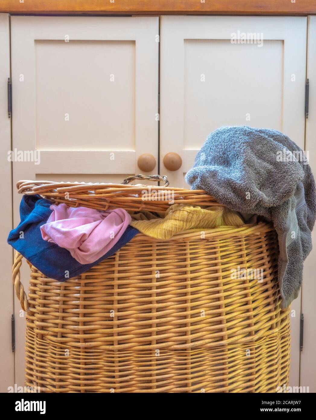 https://c8.alamy.com/comp/2CARJW7/a-full-and-overflowing-washing-laundry-wicker-basket-on-the-floor-in-front-of-a-kitchen-floor-cupboard-2CARJW7.jpg