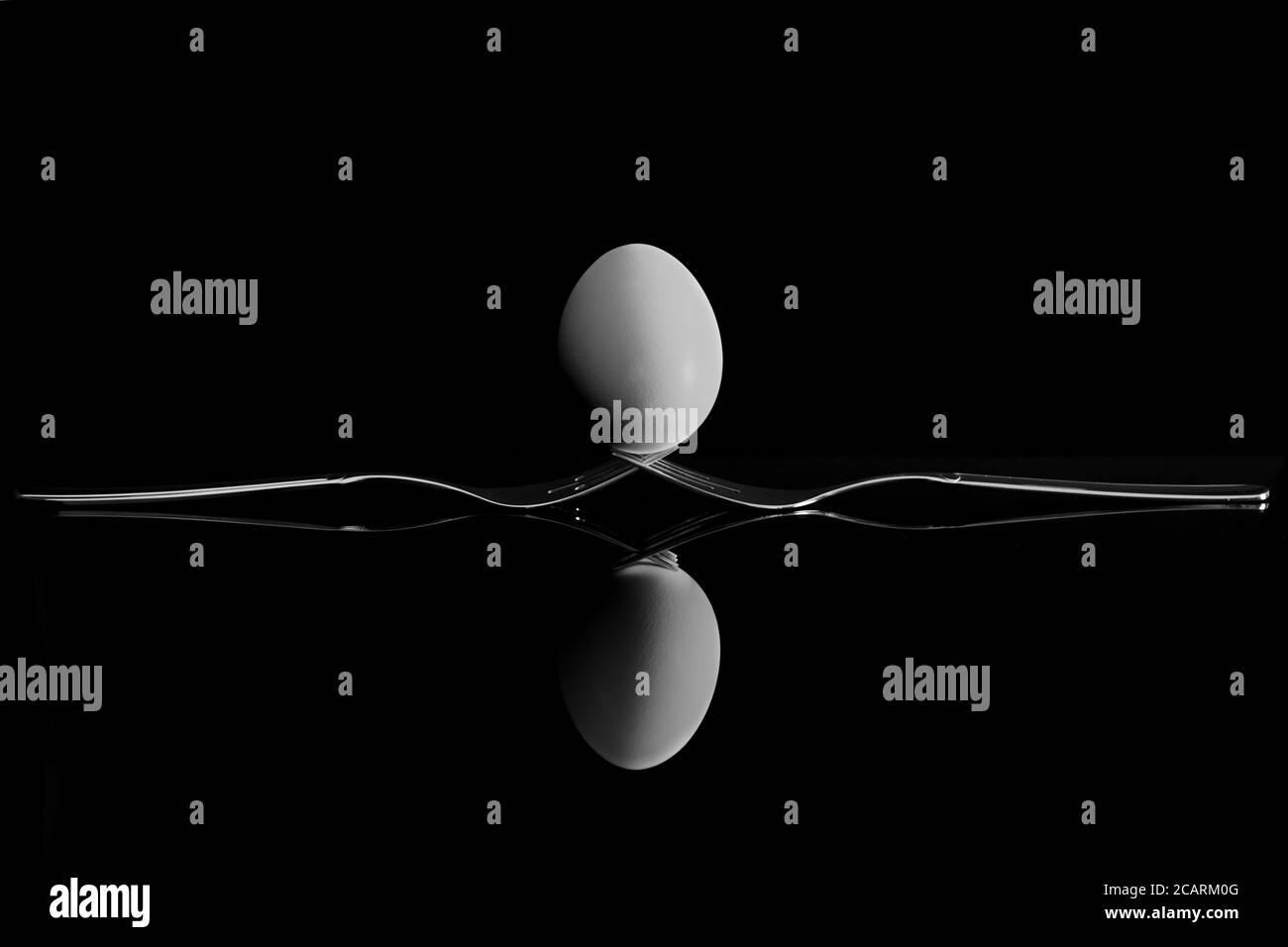 An egg balancing on two forks. Reflection on a black background. Stock Photo