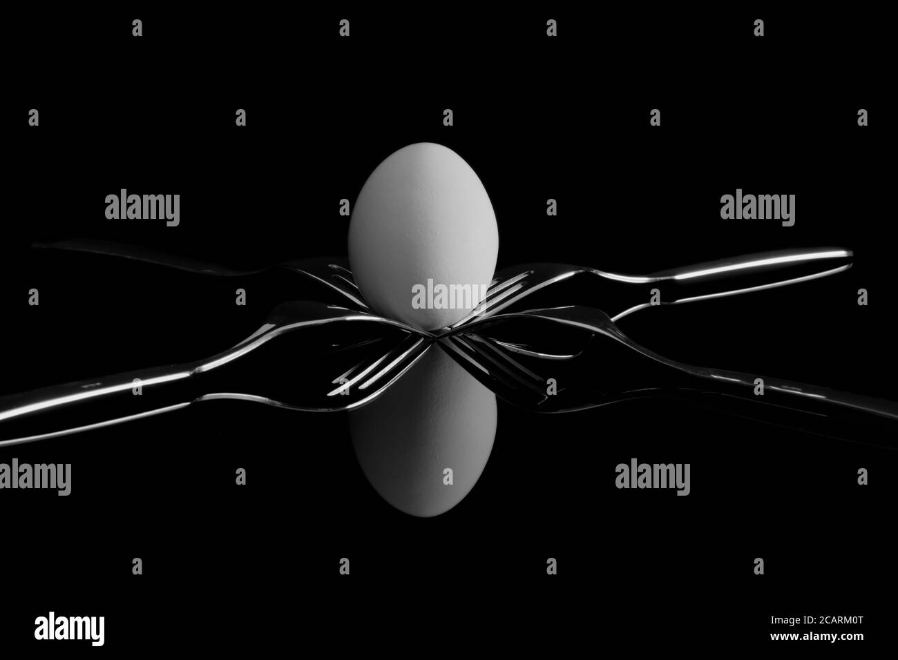 An egg balancing between four forks. Reflection on a black background. Stock Photo