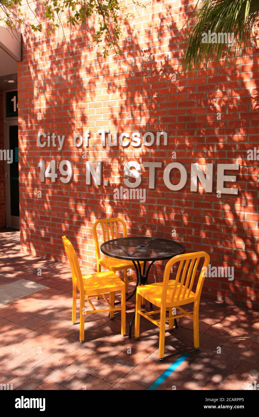 Black table and four yellow chairs outside in the mottled sunlight at 149 N Stone in downtown Tucson AZ Stock Photo