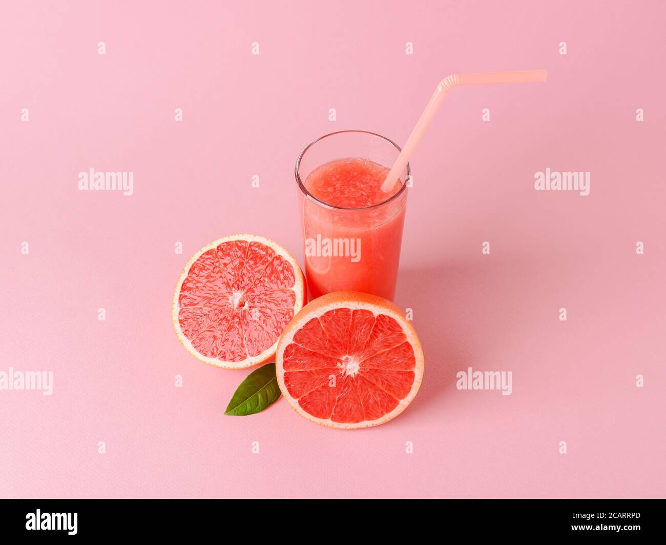 Glass of freshly squeezed grapefruit juice with pulp, drinking straw and two halves of grapefruit on a pink background. Vegetarian, raw food diet. Stock Photo