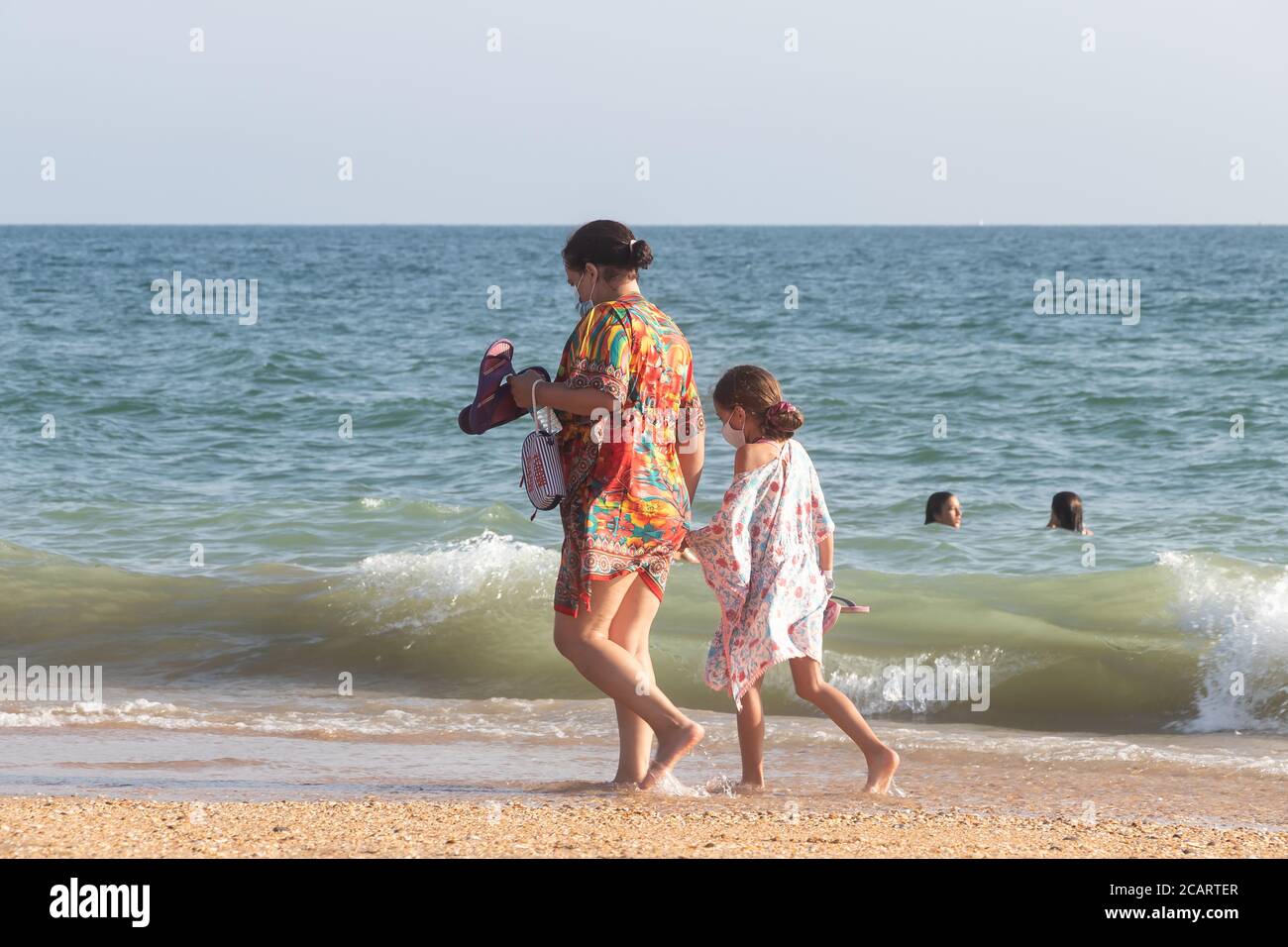 Punta Umbria, Huelva, Spain - August 7, 2020: Mother and daughter are walking by the beach wearing protective or medical face masks. New normal in Spa Stock Photo