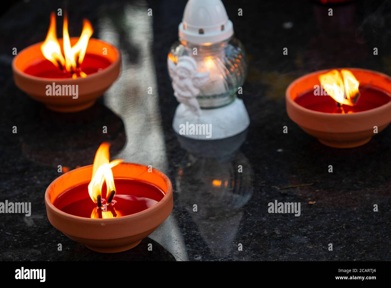 Three traditional burning grave candles and decorative one on a grave