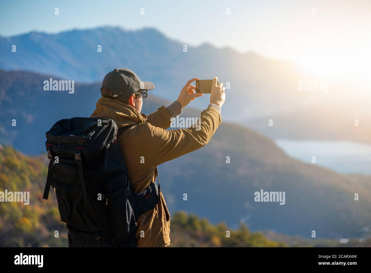 Traveler with a backpack and a smartphone stands on a mountain  Stock Photo