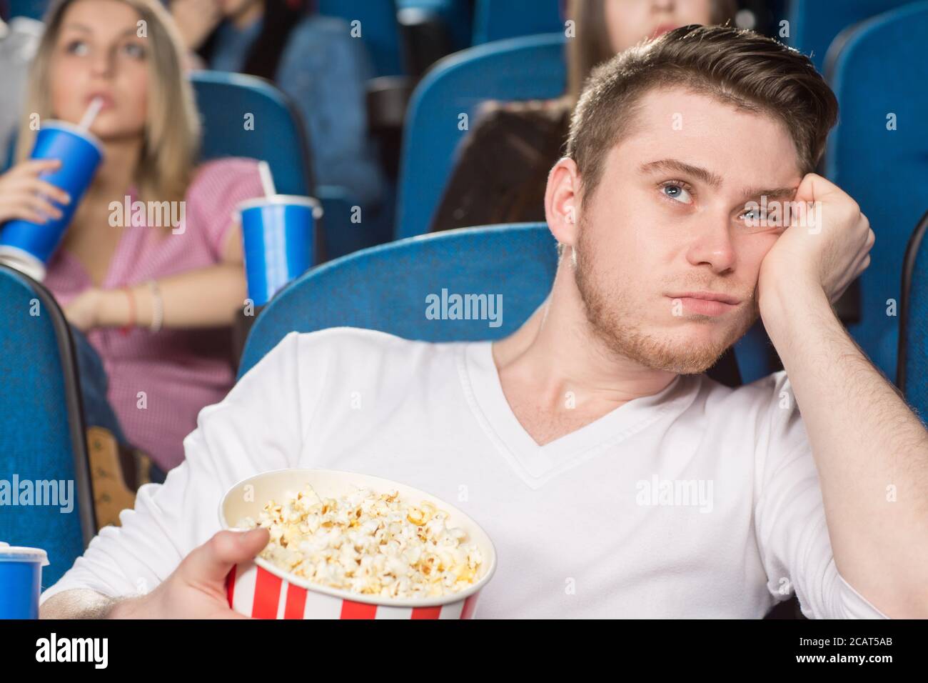 When is it ending? Shot of a young handsome man looking extremely bored watching a movie at the cinema Stock Photo