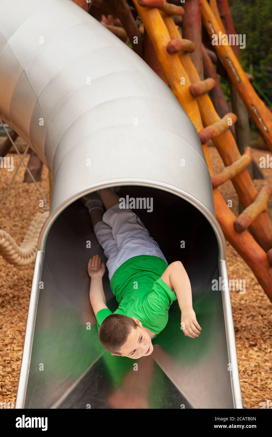 Young boy sliding down a slide in playground slide hires stock