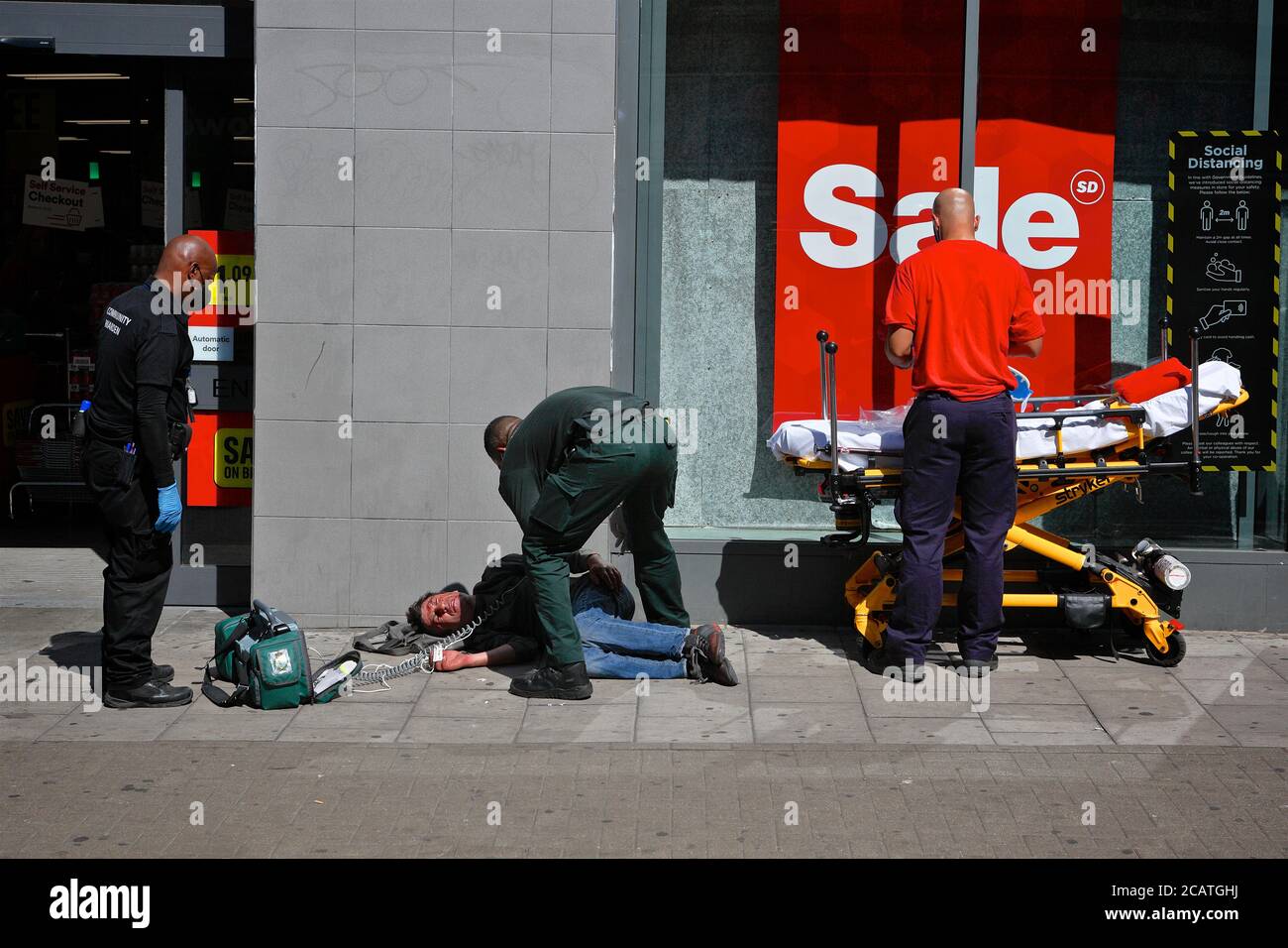 London (UK), August 7 2020: A man who has apparently collapsed on the street receives roadside medical attention. Stock Photo