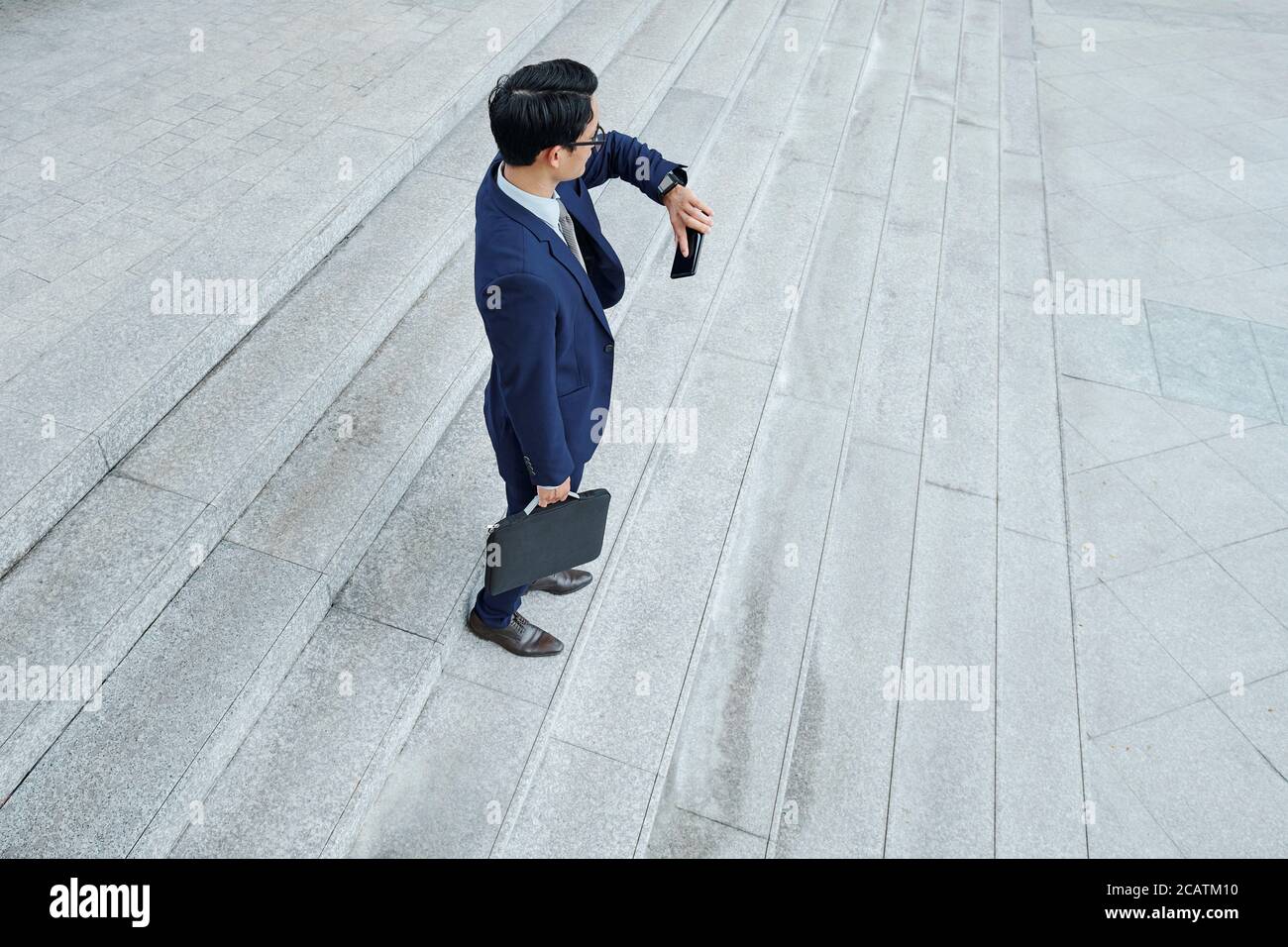 Young businessman waiting for colleague outdoors and checking time on smartwatch Stock Photo