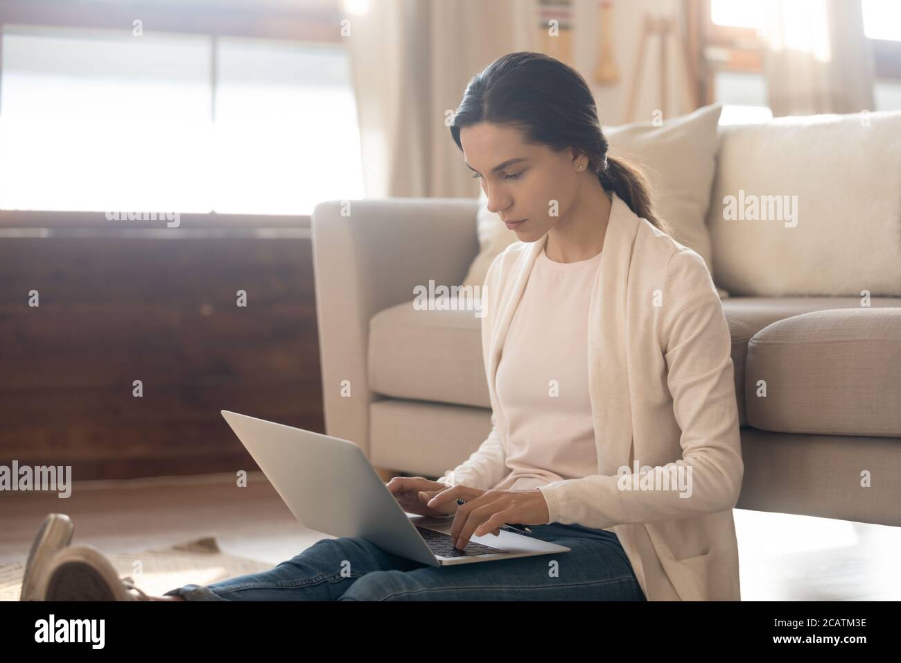 Focused young freelancer sitting on floor working remotely on computer. Stock Photo