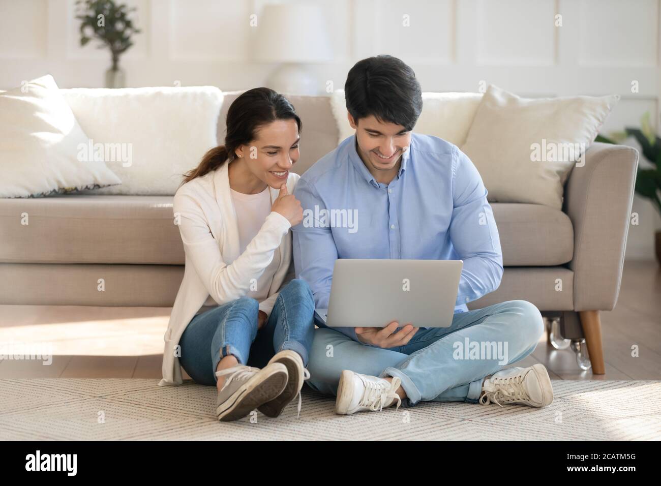 Smiling young family couple using computer together indoors. Stock Photo