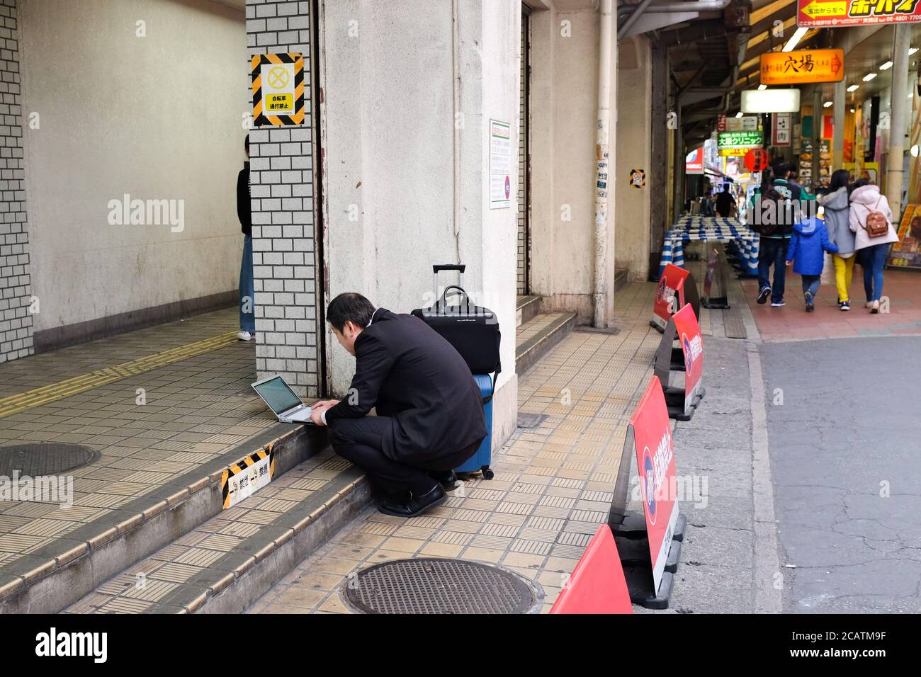 A salaryman in Japan works on his laptop while out in the street. Stock Photo