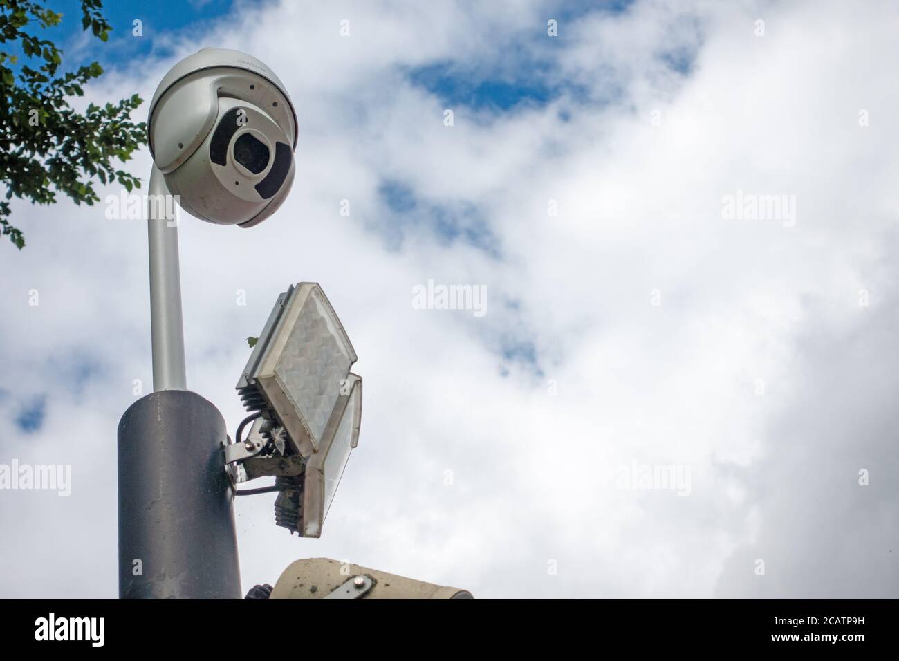 CCTV dome security camera and LED floodlight on a pole in sky Stock Photo