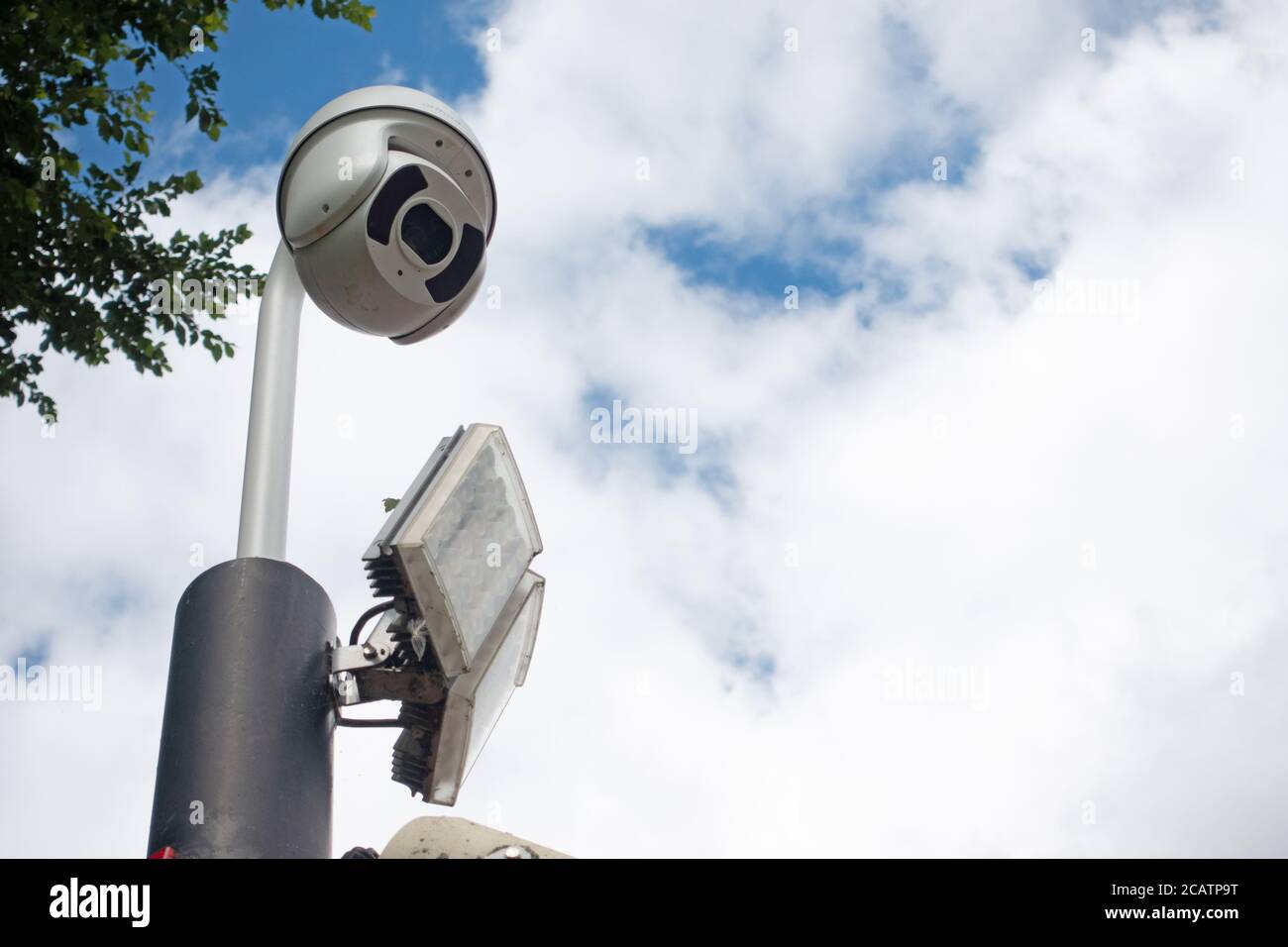 CCTV dome security camera and LED floodlight on a pole in sky Stock Photo