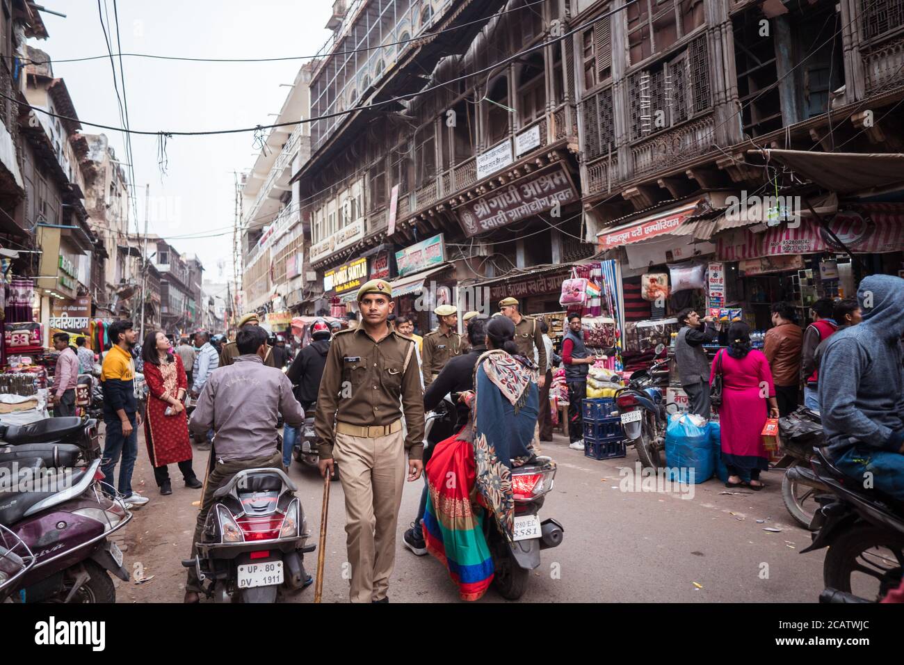 Agra / India - February 22, 2020: Environmental portrait of young military man walking holding stick through busy street in downtown Agra Stock Photo
