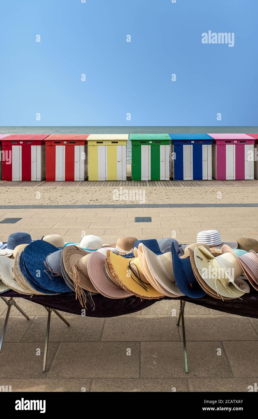 Straw hats for sale in front of multi-colored beach huts in Dunkirk, France. Stock Photo
