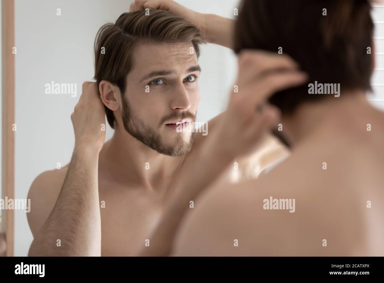 Close up anxious young man touching hair, looking in mirror Stock Photo