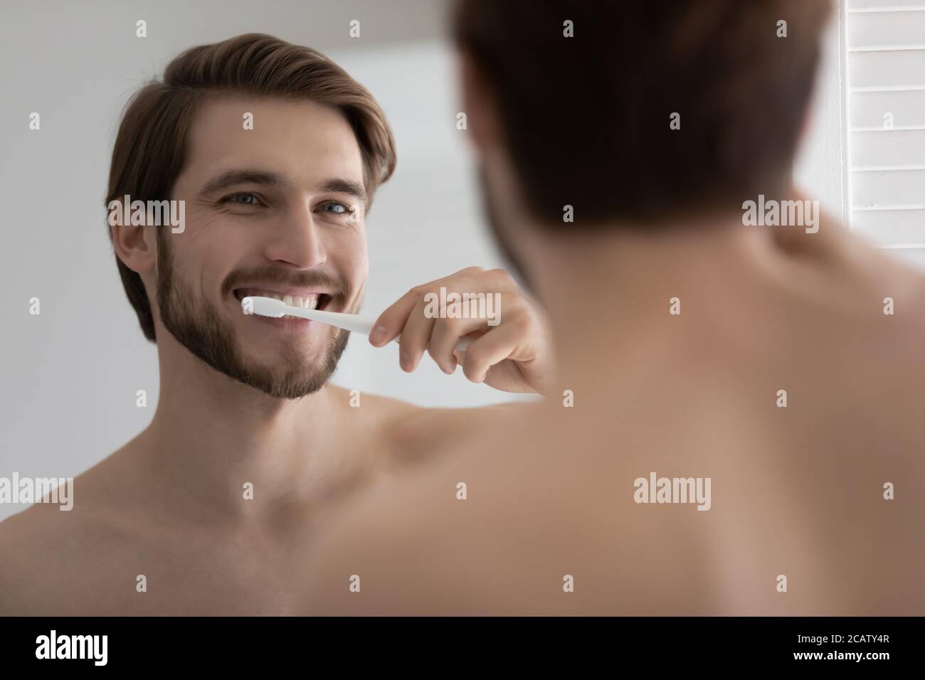 Close up mirror reflection satisfied young man brushing teeth Stock Photo