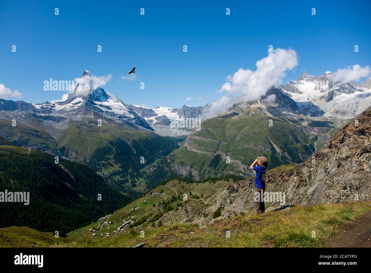 Young boy observing a bird of prey through binoculars with Swiss mountains as a backdrop. Stock Photo