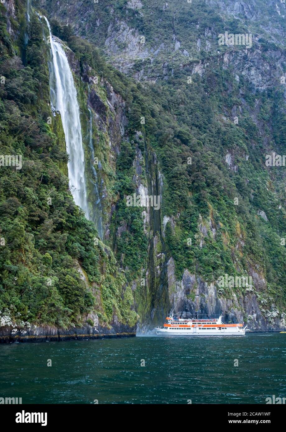Tourist boat sailing close to waterfall in famous Milford Sound Stock Photo