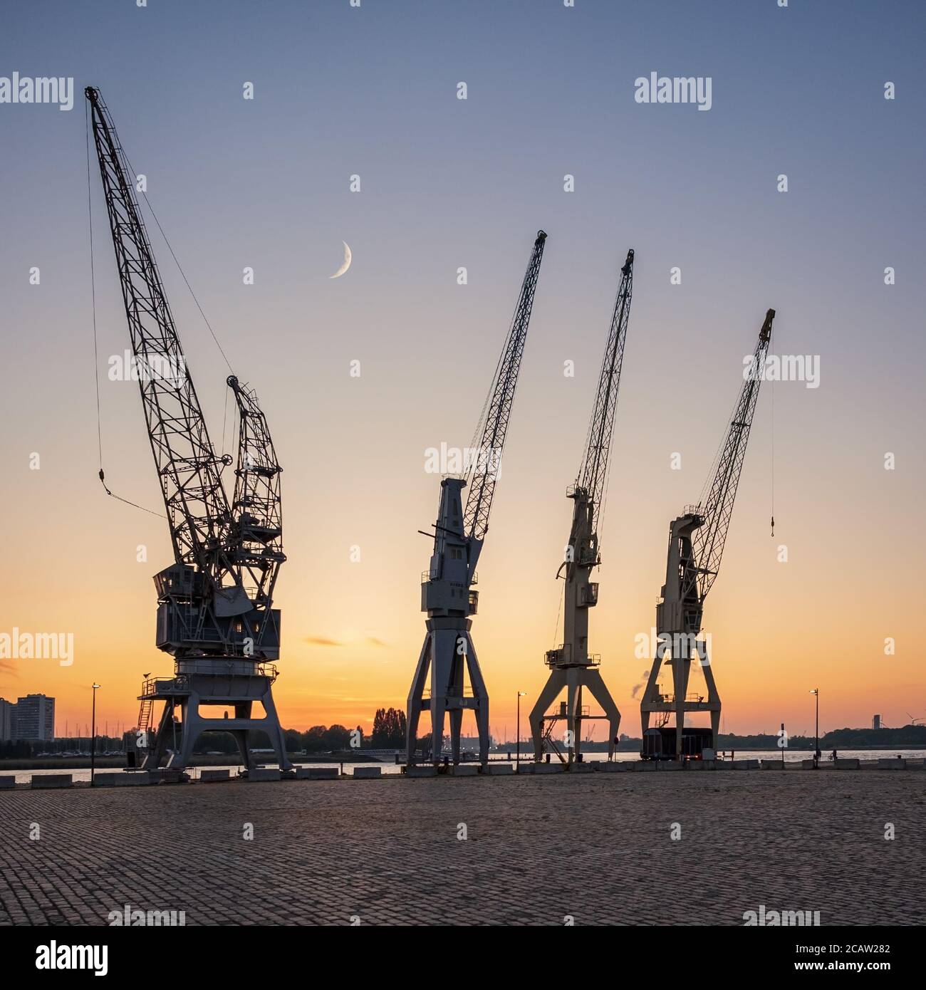 Old harbor crane silhouettes under a crescent moon. The cranes are part of the collection of the MAS museum. Stock Photo